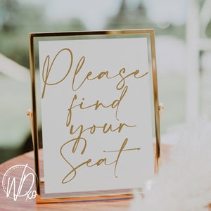 May include: A gold-framed sign with the text "Please find your seat" written in a cursive font.