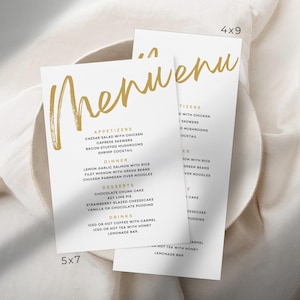 Puede incluir: Dos tarjetas de menú blancas con letras doradas, una de 12,7x17,8 cm y la otra de 10,2x22,9 cm. La palabra "Menú" está escrita en un estilo de pincel. El menú enumera aperitivos, cena, postres y bebidas.