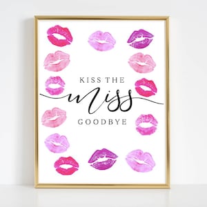 以下が含まれることがあります： 金色の枠が付いた白い印刷可能なサイン。サインの縁にはピンクと紫の唇が印刷されています。サインのテキストは「Kiss the Miss Goodbye」です。