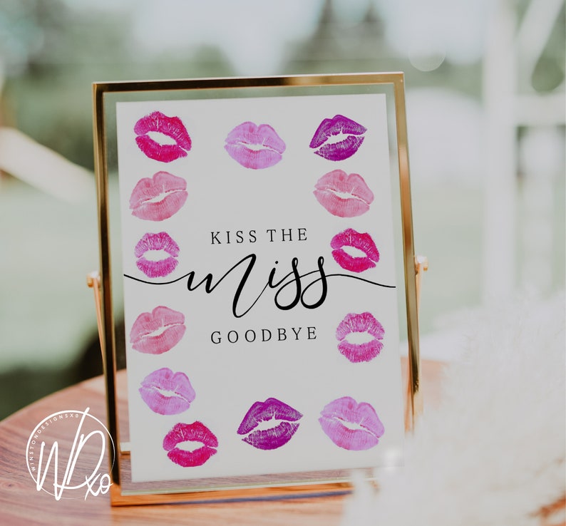 以下が含まれることがあります： 金色の額縁に入った白い看板に、黒い筆記体で「Kiss the Miss Goodbye」と書かれています。看板には、ピンクと紫の口紅のキス跡が12個あります。