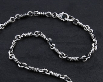 May include: A silver chain necklace with a twisted design. The chain is made of small, round links that are twisted together to create a unique look.
