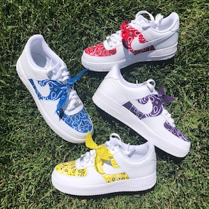 May include: Four white sneakers with custom bandana designs in red, blue, purple, and yellow. Each shoe features a different color bandana pattern on the Nike swoosh and toe area, with matching bandana laces.