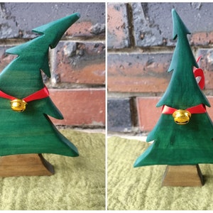 May include: A wooden Christmas tree ornament painted green with a red ribbon and a gold bell. The tree is standing on a wooden base.