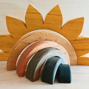 Pode incluir: Conjunto de brinquedos de madeira com design de girassol e arco-íris. O girassol tem pétalas amarelas, e o arco-íris consiste em arcos em tons de castanho, verde e cinza. Um brinquedo criativo e educativo.