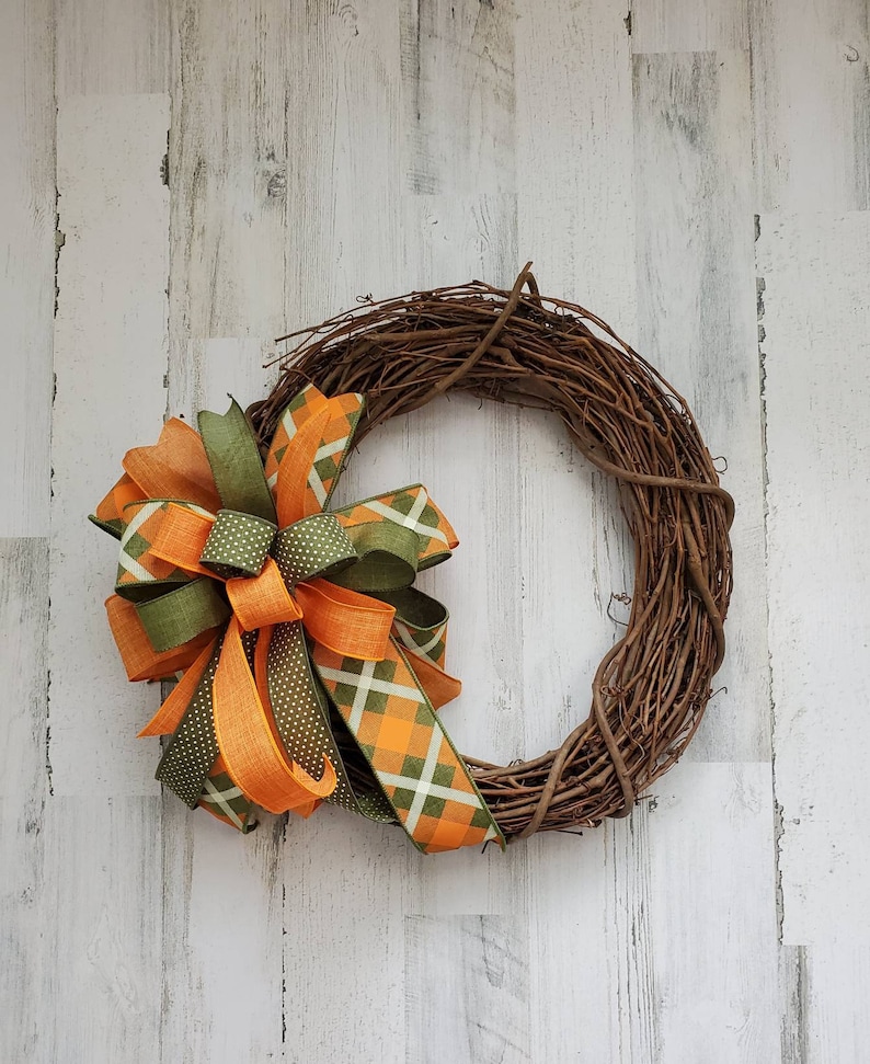 May include: A grapevine wreath with a large bow made of orange and green plaid ribbon. The bow is tied with a green ribbon with white polka dots.