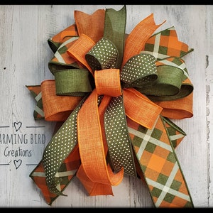 May include: A large, multi-layered bow made with orange and green patterned ribbon. The bow is tied with a knot in the center and has a rustic, farmhouse style.