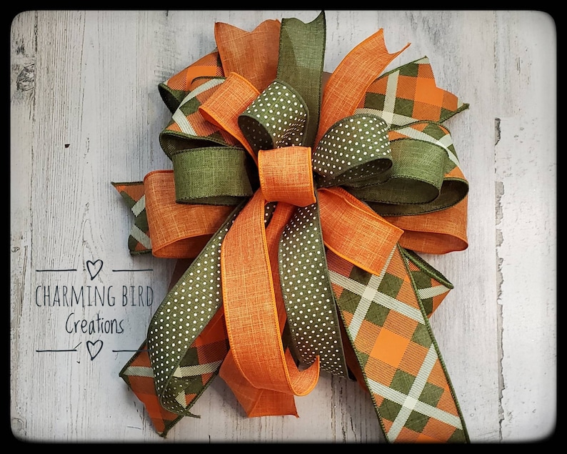 May include: A large, multi-layered bow made with orange and green patterned ribbon. The bow is tied with a knot in the center and has a rustic, farmhouse style.