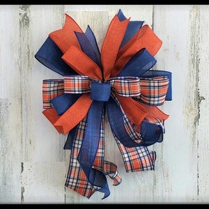 May include: A large bow made with three different ribbons. The bow is made with a red ribbon, a blue ribbon, and a plaid ribbon with red, blue, and white squares. The bow is tied with a knot in the center.