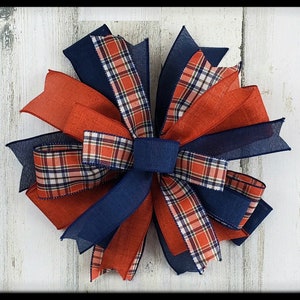 May include: A large bow made with red, white, and blue plaid ribbon and navy blue ribbon. The bow is tied in a knot and has a layered look.