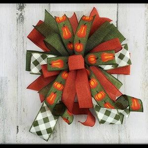 May include: A fall-themed bow with green, red, and white ribbon. The ribbon has a checkered pattern and a pumpkin print.