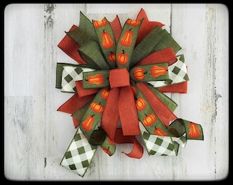 May include: A fall-themed bow with green, red, and white ribbon. The ribbon has a checkered pattern and a pumpkin print.