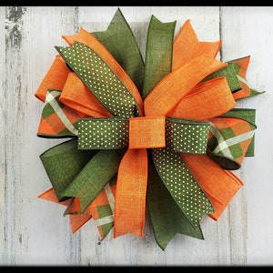 May include: A large, decorative bow made with orange and green ribbon. The bow has a plaid pattern, polka dots, and a solid green ribbon in the center.