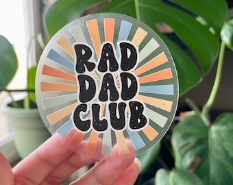 May include: Clear sticker with a retro sunburst design in shades of orange, yellow, and blue. The text "RAD DAD CLUB" is in black with a distressed look.