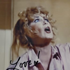 May include: A vintage photograph of a woman with blonde curly hair, blue eyes, and an open mouth, looking upwards with an expression of surprise or fear. The word "Love!" is written in cursive at the bottom left.
