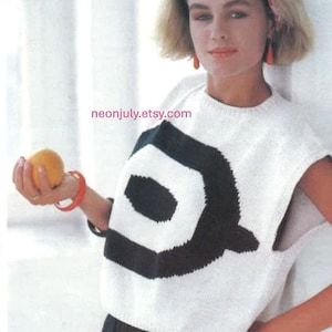 Könnte beinhalten: Weißes ärmelloses Strickoberteil mit großem schwarzem geometrischen Design. Der Text "Spring and summer 7 Target motif sweater" ist sichtbar. Die Person trägt schwarze Shorts und hält eine Orange.