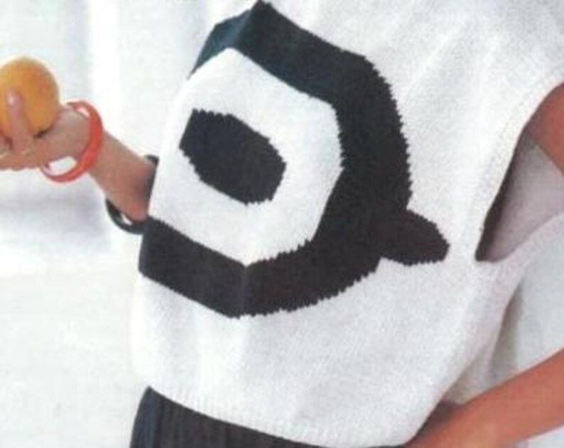 Puede incluir: Un su&eacute;ter blanco sin mangas con un gran dise&ntilde;o geom&eacute;trico negro en la espalda. El su&eacute;ter est&aacute; hecho de un material de punto. Una persona sostiene una fruta naranja y lleva una pulsera roja.