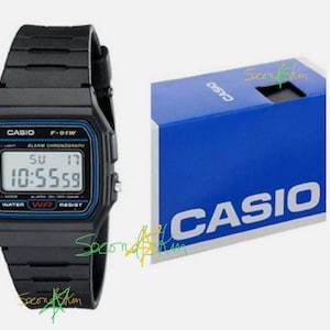 May include: A black Casio F-91W digital watch with a black resin band. The watch face displays the time, date, and day of the week. The watch is in its original packaging, which is a blue box with the Casio logo.