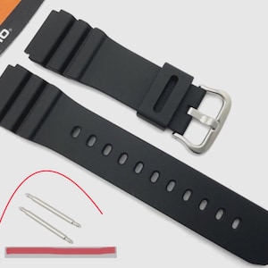 May include: Black watch band replacement with a silver buckle. The band has a ribbed texture and multiple holes for adjustment. Includes two silver pins and a red adhesive strip. The Casio logo is visible in the background.