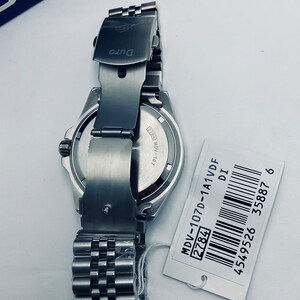 May include: A silver watch with a stainless steel strap and a black face. The watch has a date window and a silver clasp. The watch is on a white background with a white tag that says "MDV-107D-1A1VDF 2784 DI 4549526 35887 6".