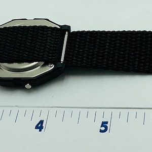 May include: A black watch with a black nylon strap. The watch is about 4 inches long and has a silver case. The strap has the text "COOL & DRY" printed on it.