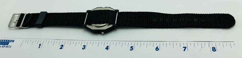 May include: A black watch with a black nylon strap. The watch is about 4 inches long and has a silver case. The strap has the text "COOL & DRY" printed on it.