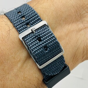 May include: A dark gray woven watch strap with a silver buckle and a black rubber keeper.