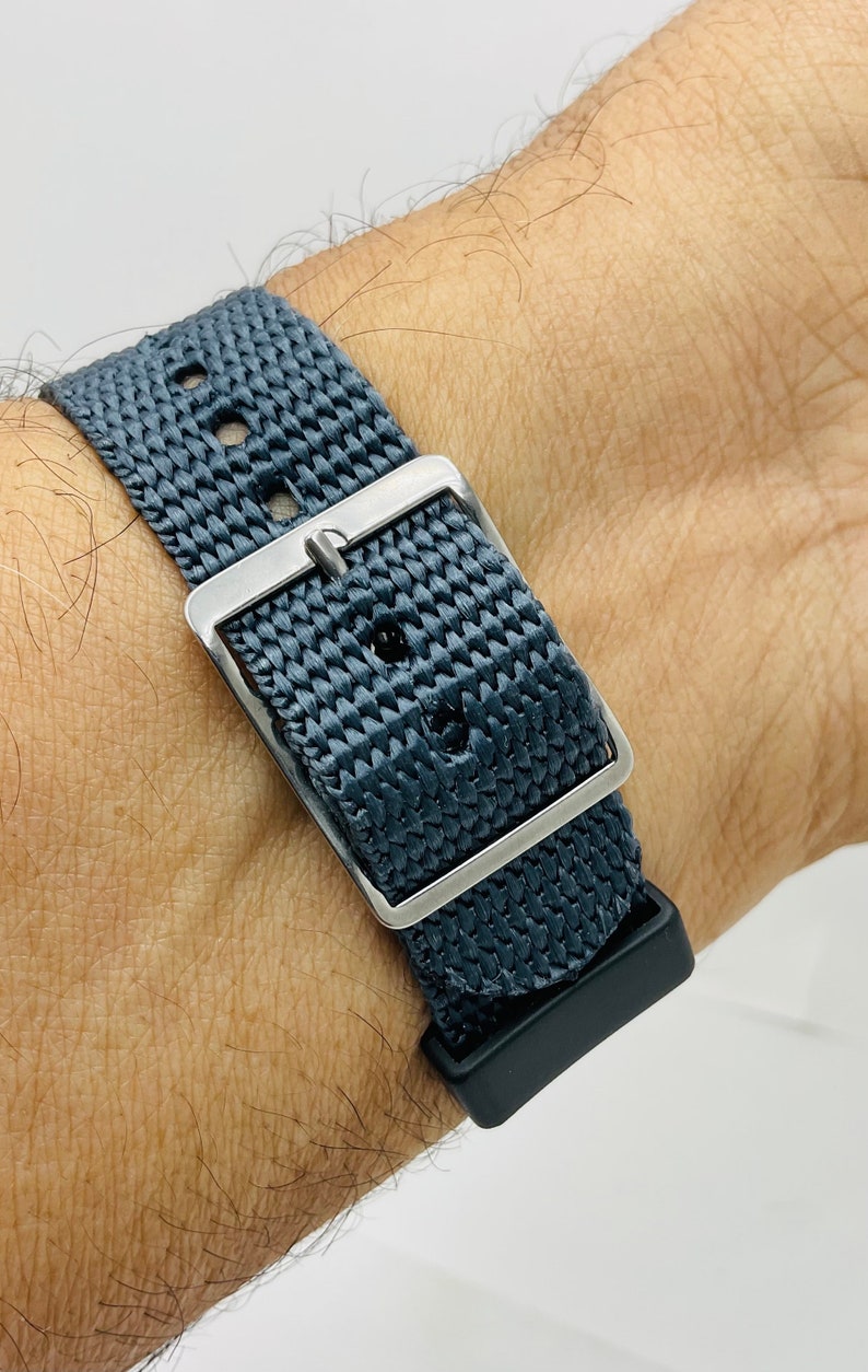 May include: A dark gray woven watch strap with a silver buckle and a black rubber keeper.