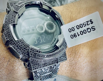 Könnte beinhalten: Eine silberfarbene Casio Digitaluhr mit einer schwarz eingelegten Lünette und Armband. Das Zifferblatt zeigt die Uhrzeit 3:32:42 an. Die Uhr hat eine Digitalanzeige und mehrere Knöpfe. Die Uhr befindet sich an einem Handgelenk.