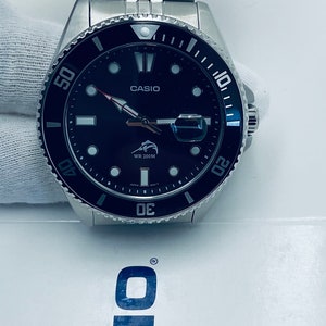 May include: A black and silver Casio wristwatch with a black face and white markings. The watch has a silver metal band and a rotating bezel with blue markings. The watch face features a white Casio logo, a white fish logo, and the text "WR 200M".