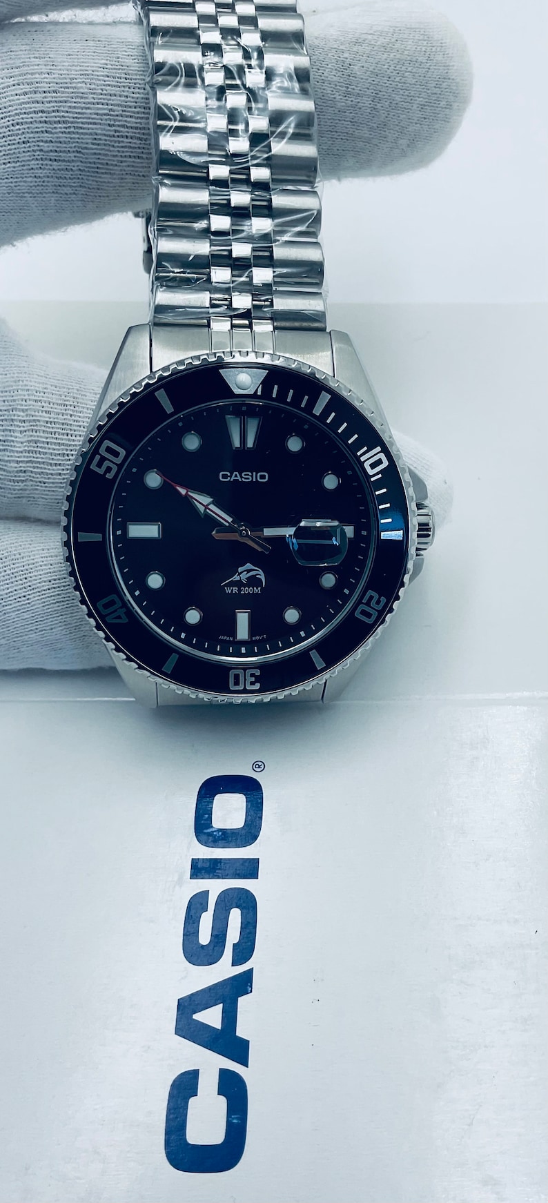 May include: A black and silver Casio wristwatch with a black face and white markings. The watch has a silver metal band and a rotating bezel with blue markings. The watch face features a white Casio logo, a white fish logo, and the text "WR 200M".