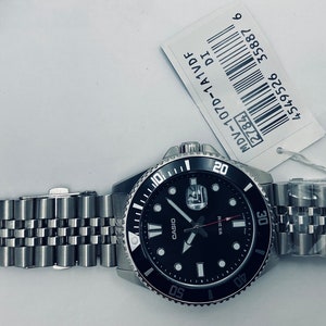 May include: A black and silver Casio watch with a black face and silver hands. The watch has a black bezel with white markings and a silver metal band. The watch is labelled "MDV-107D-1A1VDF" and has a barcode.