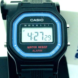 May include: A black Casio digital watch with a blue face and a black band. The watch has a digital display showing the time, date, and alarm. The watch is water resistant and has a timer function.