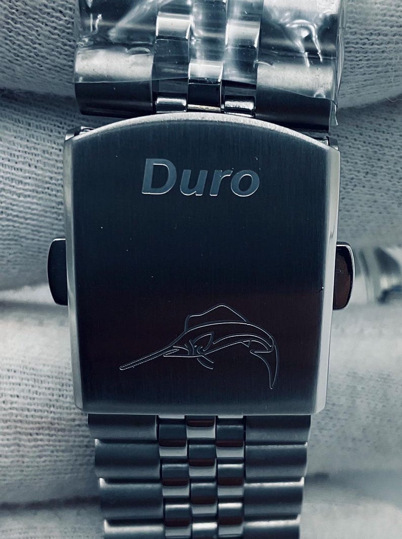 May include: A silver watch strap with a silver clasp. The clasp has the word "Duro" engraved on it and a small marlin fish design.