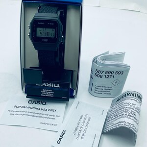 May include: A black Casio F-91W digital watch with a black strap, displayed in its original blue box. The watch face shows the time. Included are warranty cards and a warning label. The watch is water-resistant.