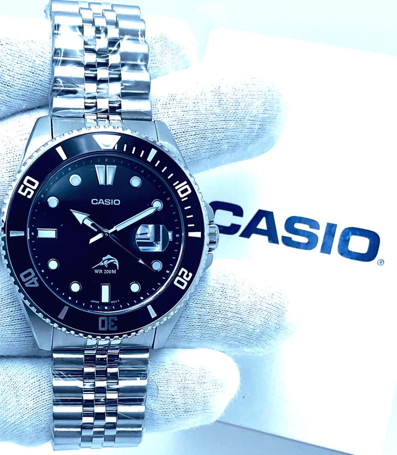 May include: A silver Casio wristwatch with a black face and a silver metal band. The watch has a black bezel with white markings and the words "WR 200M" on the face. The watch is on a white background with the word "CASIO" in blue letters.