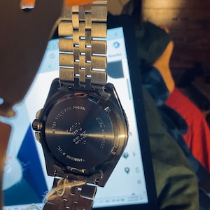 May include: A silver watch with a stainless steel strap. The watch face is black with white markings. The back of the watch has the text "WATER RESIST 20BAR" and "CASIO" printed on it.