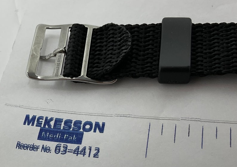 May include: A black woven watch strap with a silver buckle that says "Stainless Steel".