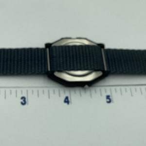 May include: A gray nylon watch strap with a silver watch face. The strap is 8 inches long.
