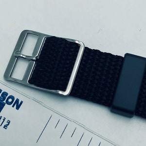 May include: A black nylon watch strap with a silver buckle. The strap has a black keeper and is designed for a watch with a 20mm lug width.