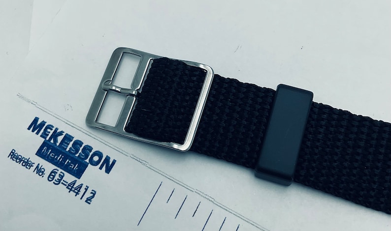 May include: A black nylon watch strap with a silver buckle. The strap has a black keeper and is designed for a watch with a 20mm lug width.