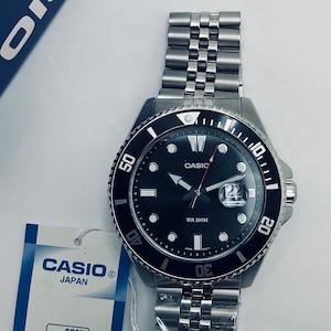 May include: A black Casio wristwatch with a silver metal strap. The watch face has a black background with white markings and a date window. The watch is water resistant to 200 metres.
