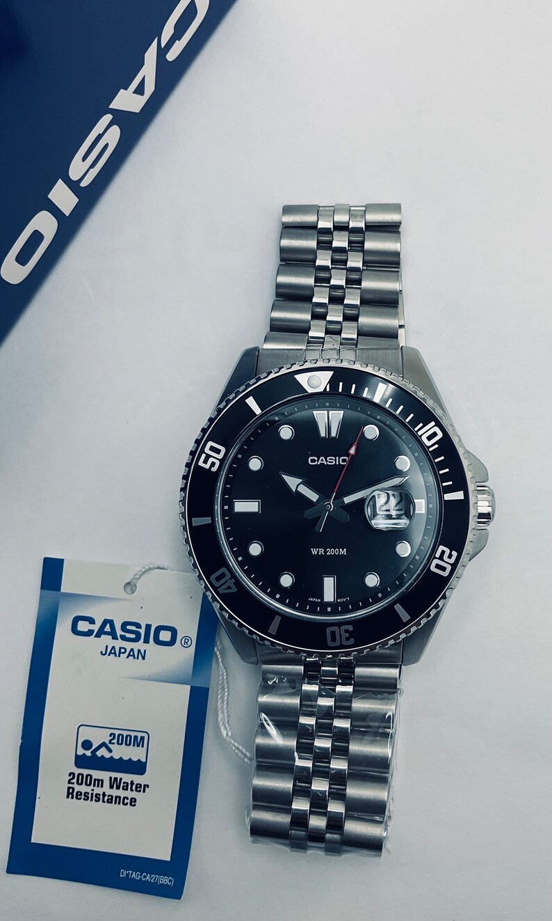 May include: A black Casio wristwatch with a silver metal strap. The watch face has a black background with white markings and a date window. The watch is water resistant to 200 metres.