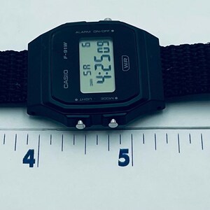 May include: Black digital watch with a black fabric band. The watch face displays the time 4:25:09. The band is approximately 8 inches long. The watch has a silver buckle.