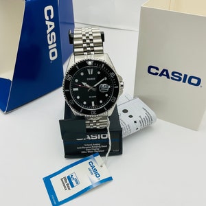 May include: A silver Casio watch with a black face and a silver metal strap. The watch features a date display and is water resistant to 200 metres. The watch is in a box with a Casio logo.