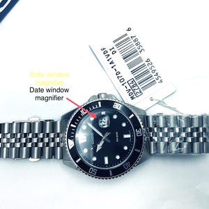 May include: A black Casio wristwatch with a silver metal band. The watch face has a black background with white markings and a date window with a magnifier. The watch has a rotating bezel with numbers and markings.