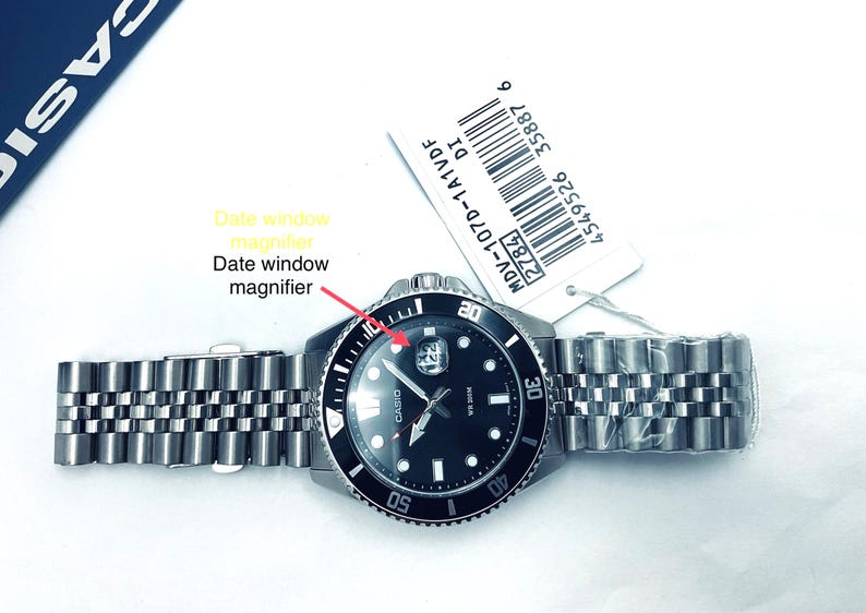 May include: A black Casio wristwatch with a silver metal strap. The watch face has a black background with white markings and a date window with a magnifier. The watch has a rotating bezel with numbers and markings.