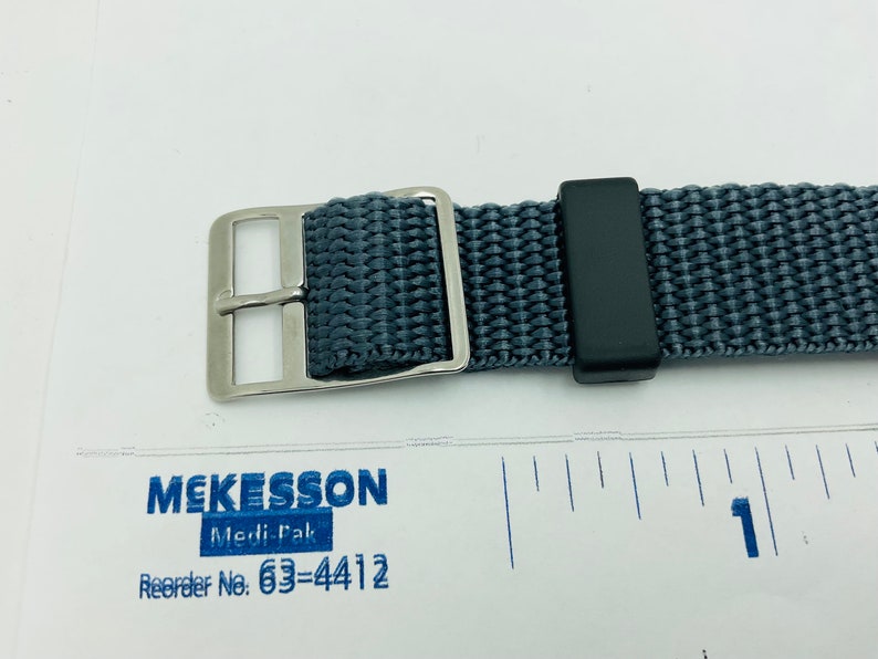 May include: A gray nylon watch strap with a silver buckle and a black keeper. The strap is about 1 inch wide.