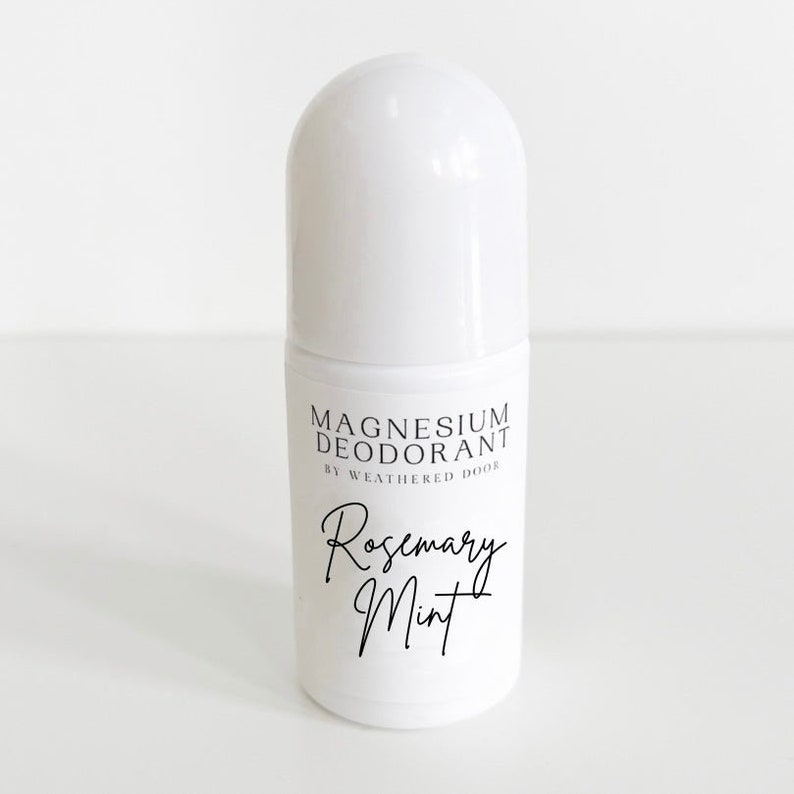 Pode incluir: Frasco de desodorizante roll-on branco com um r&oacute;tulo preto que diz "Magnesium Deodorant by Weathered Door Rosemary Mint".