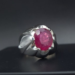 Puede incluir: Un anillo de plata con una gran piedra preciosa de rubí de forma ovalada engastada en un engaste decorativo y ornamentado.