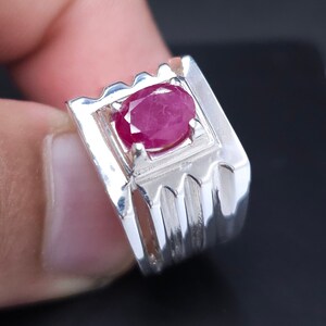 Puede incluir: Un anillo de plata con una piedra ovalada roja engastada en un marco cuadrado. El anillo tiene una banda texturizada.
